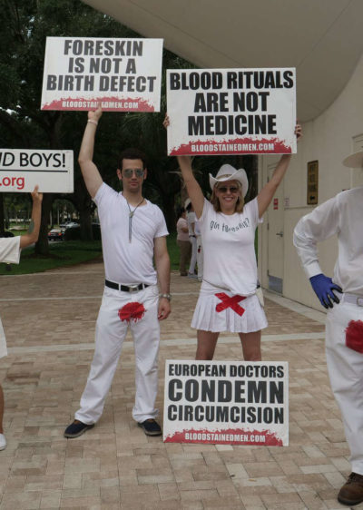Protesters hold many signs, including "Foreskin is not a Birth Defect", "Blood Rituals are not Medicine", and "European Doctors Condemn Circumcision"