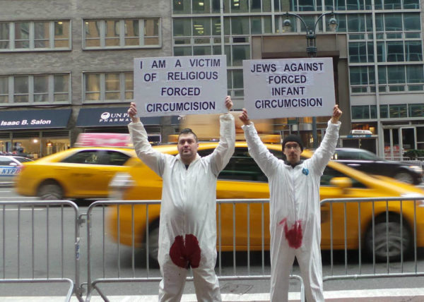 Two bloodstained men in New York City hold protest signs – "I am a Victim of Religious Forced Circumcision" and "Jews Against Forced Infant Circumcision"